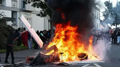 Getty Images An enormous fire is seen outside a school as protesters look on from behind