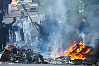 Getty Images A road sign is hurled into burning wreckage in the street by a masked and hooded man