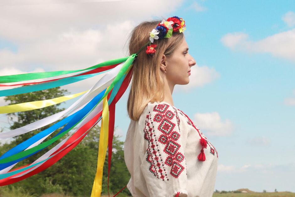 Portrait of Ukrainian young girl in profile view in national costume with wreath on her head on background of field with poppies and blue sky . Ethnic Ukrainian costume. Patriotic themes
