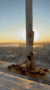 a rusty railing with a city in the background at sunset